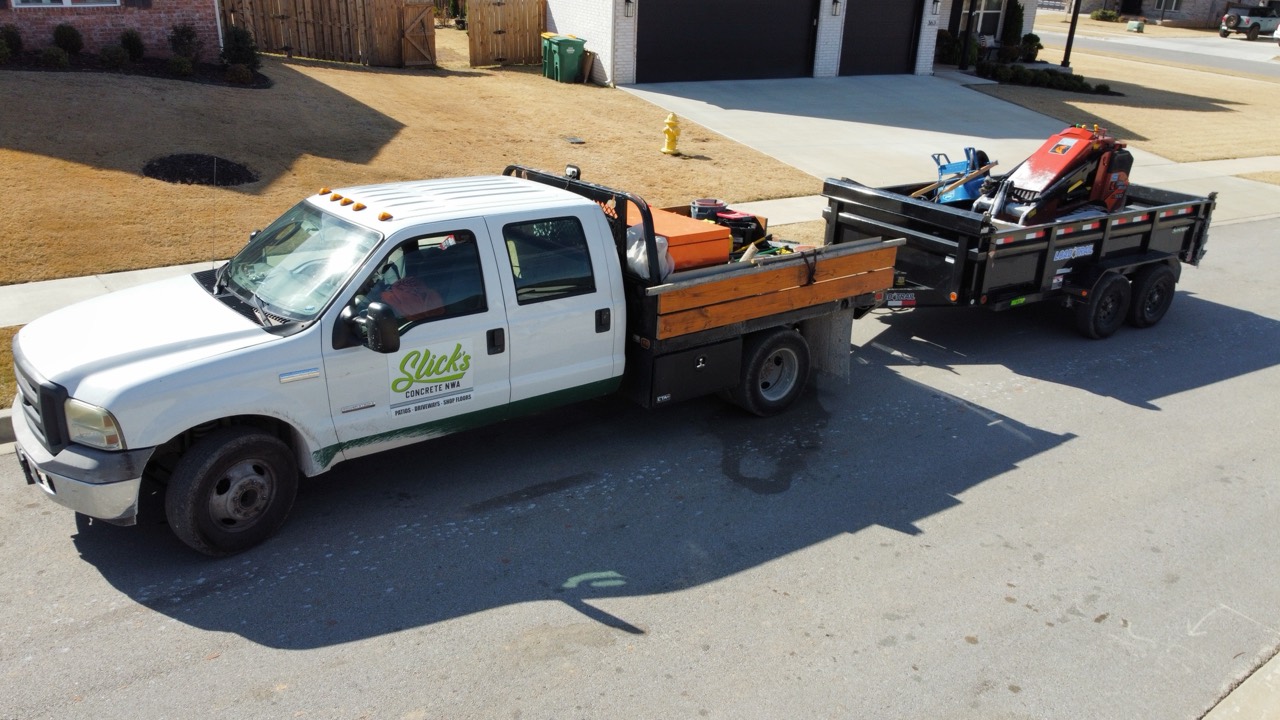A newer Slick's Concrete work truck towing a loaded equipment trailer