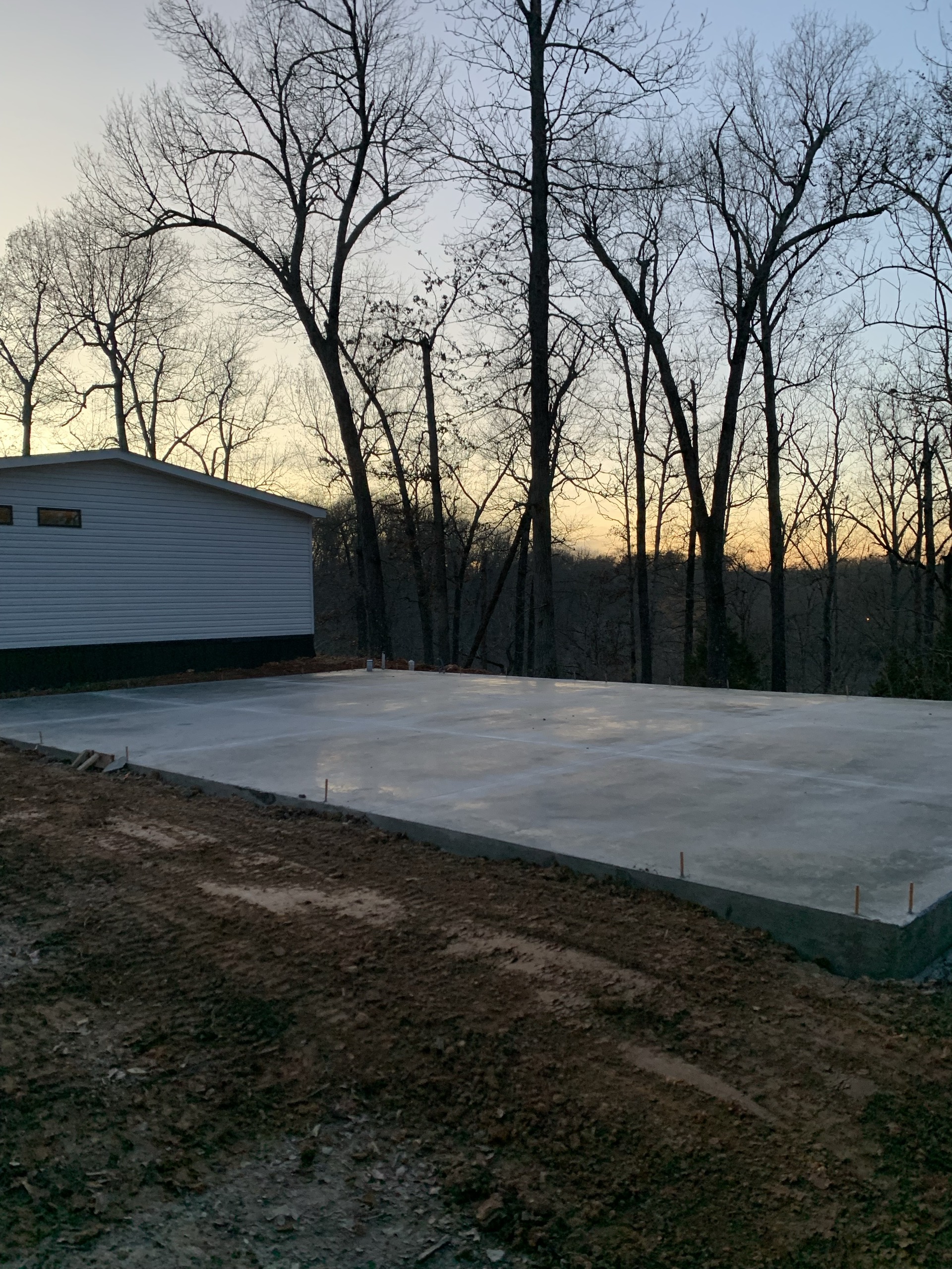 A large finished concrete slab at dusk beside a wooded hillside